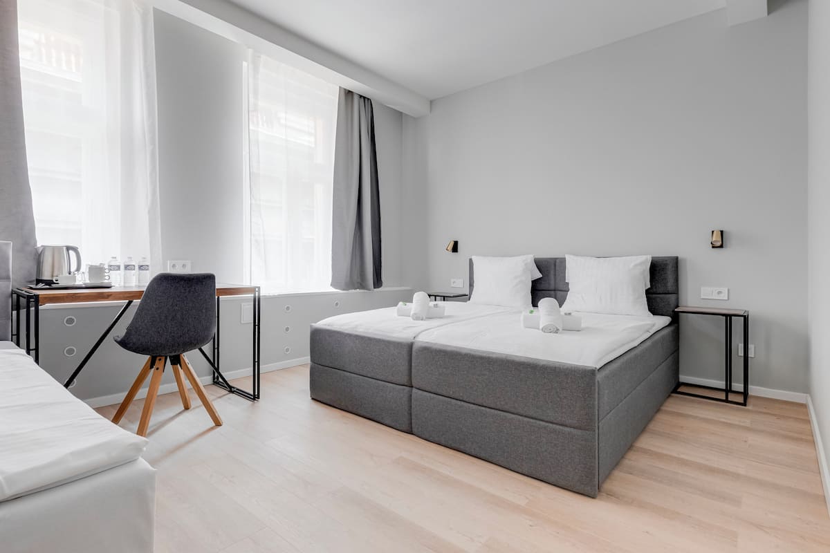 A modern hotel room with a large bed, a desk with a chair, and a window with curtains.