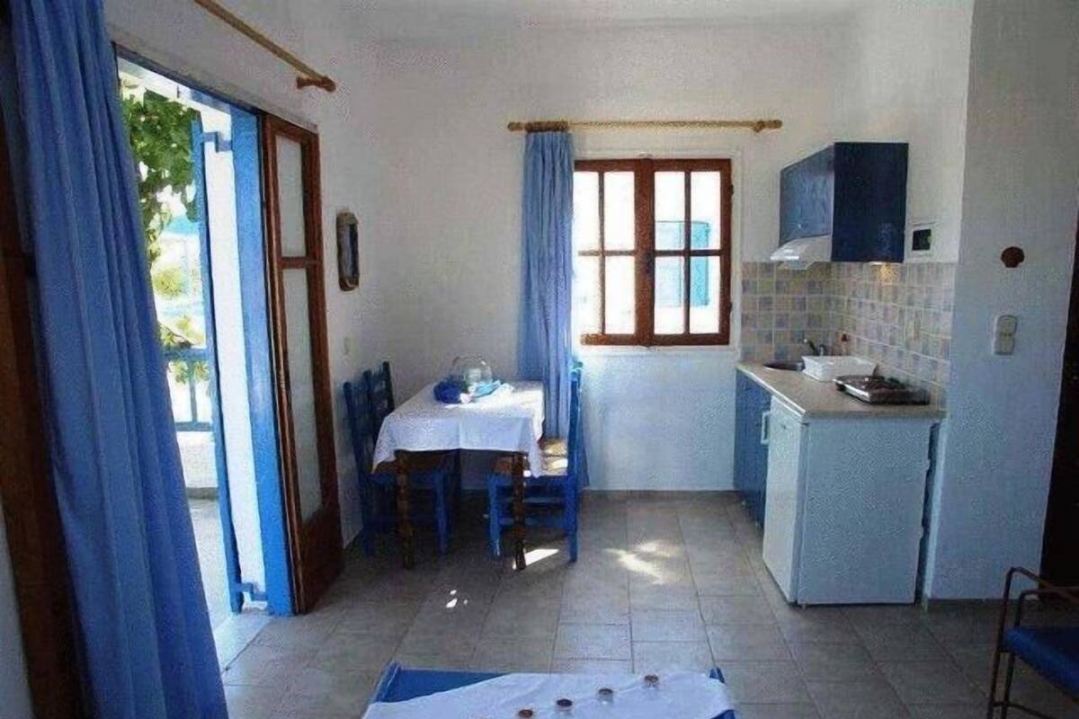 A compact kitchen with a dining table and chairs, a small refrigerator, and a window with curtains.