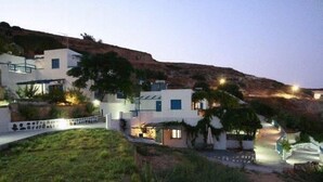 Una propiedad en una colina con edificios blancos, un camino de entrada pavimentado y un muro de piedra.