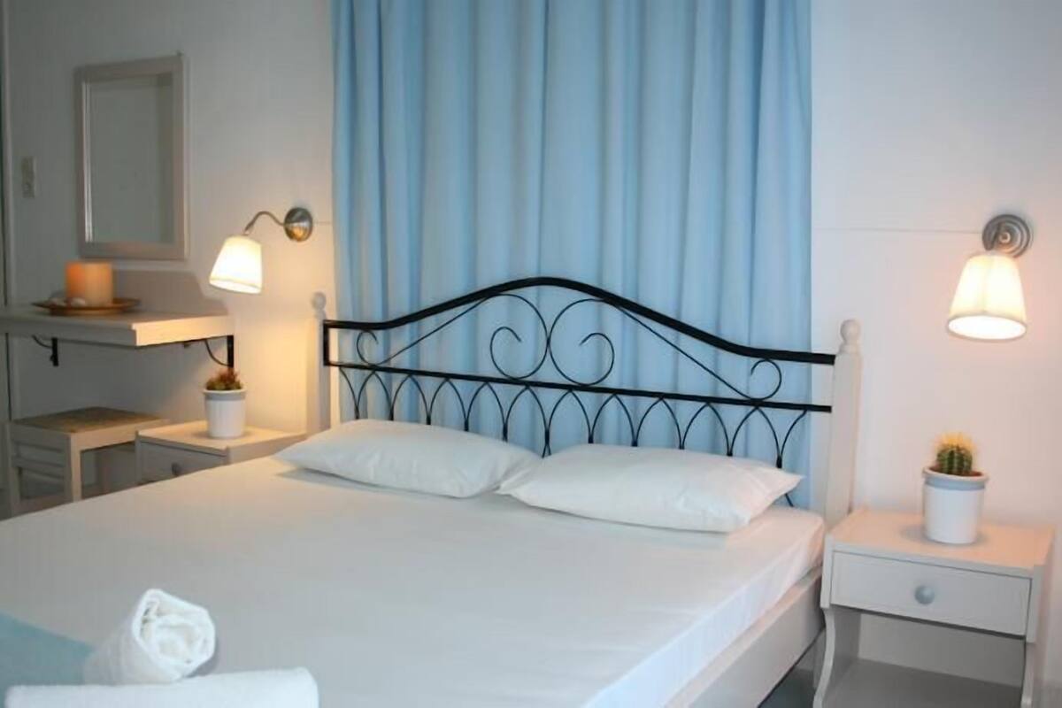 A neatly made bed with white linens, a black metal headboard, and two bedside lamps.