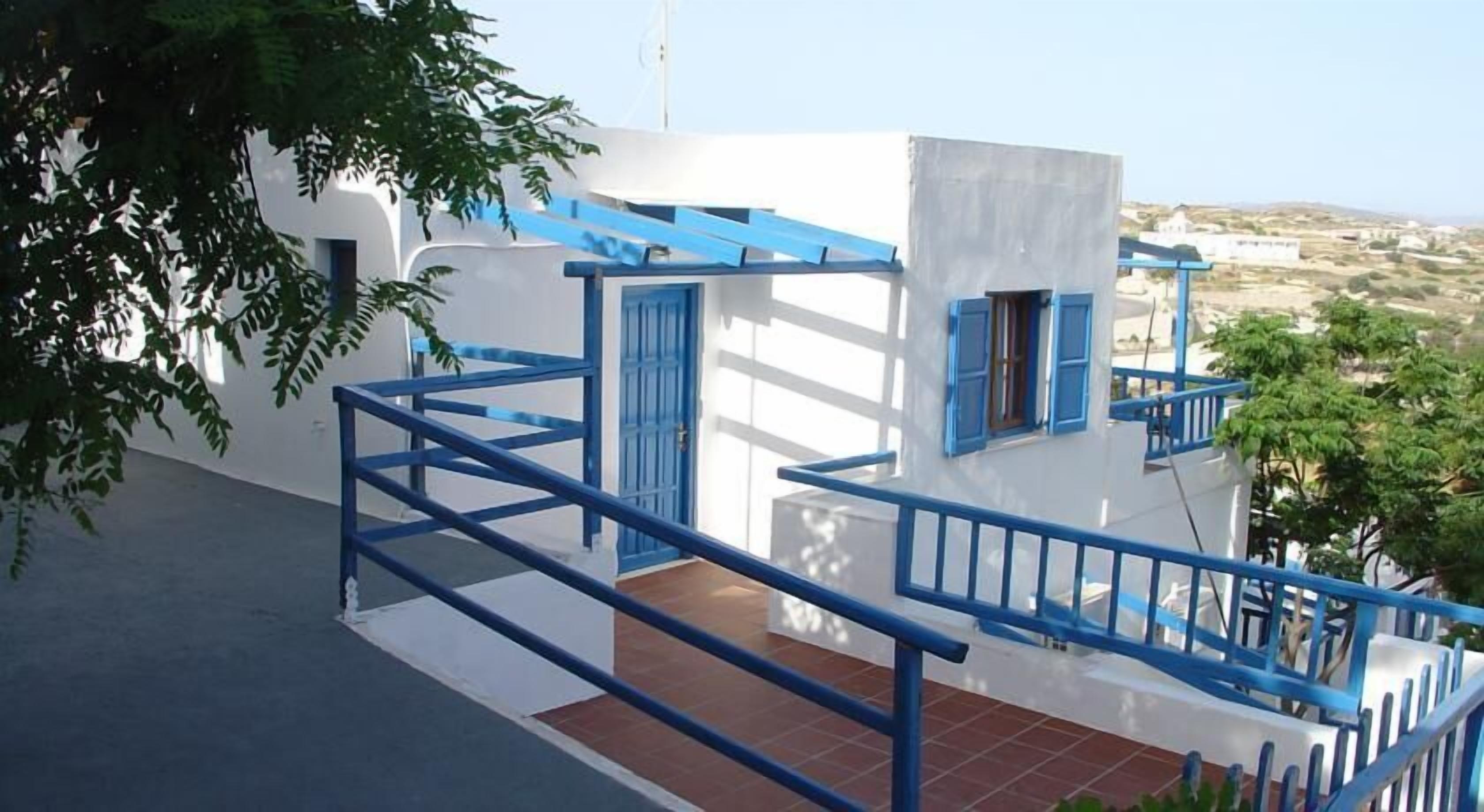 Un edificio blanco con detalles azules, una escalera y vistas a un paisaje montañoso.