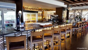 Een bar met een lange toonbank, meerdere barkrukken en een koelkast vol drank.