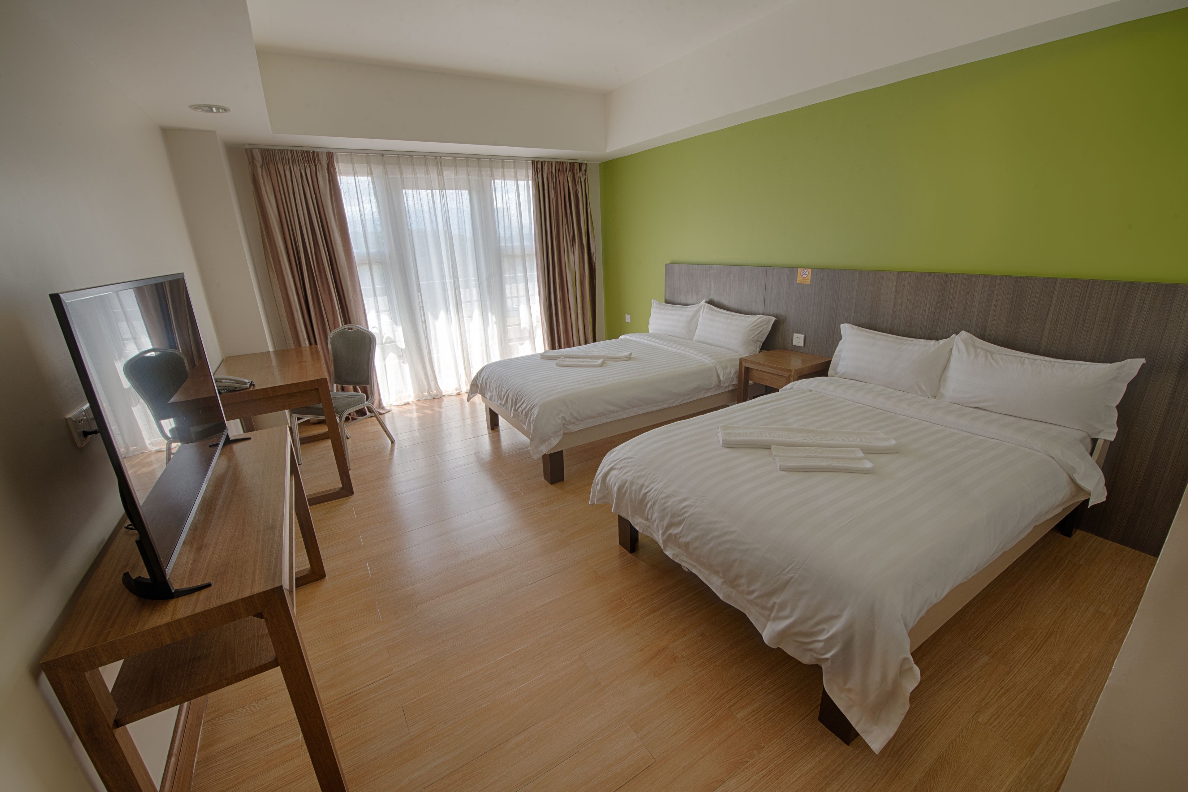 A hotel room with two beds, a desk with a chair, a television, and a window with curtains.