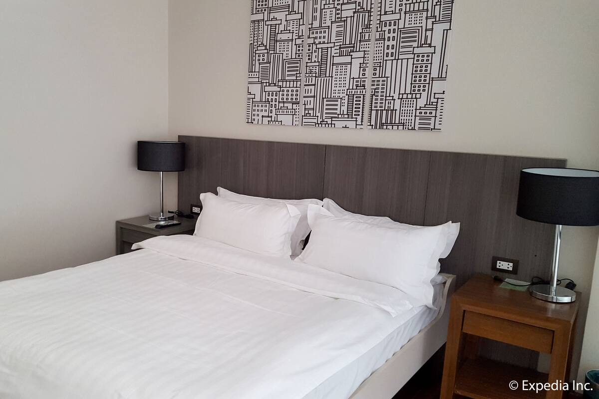 Een hotelkamer met een net opgemaakt bed, een nachtkastje met een lamp en een kunstwerk aan de muur.