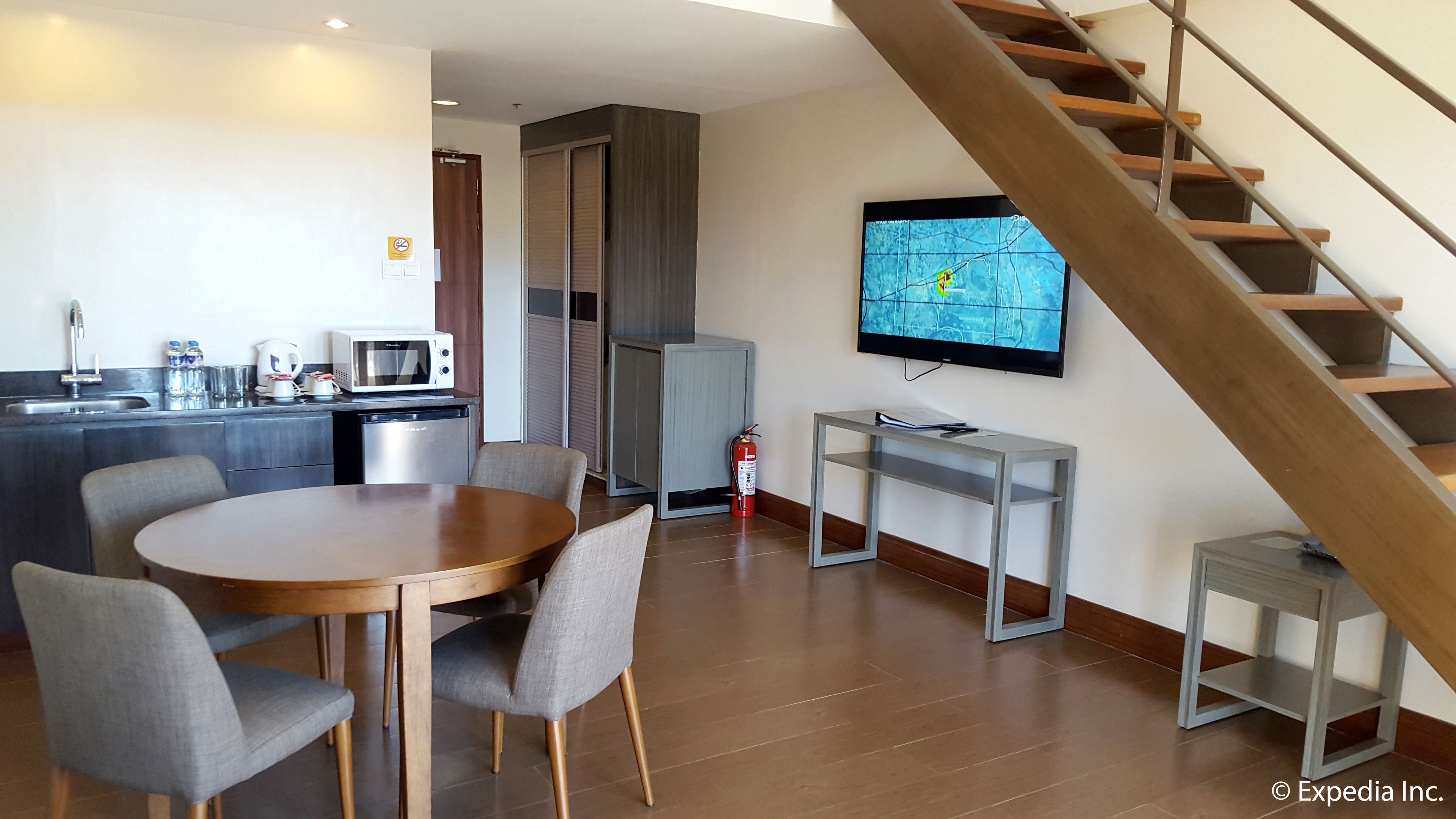 Una habitación de hotel moderna con zona de comedor, kitchenette y televisor montado en la pared.
