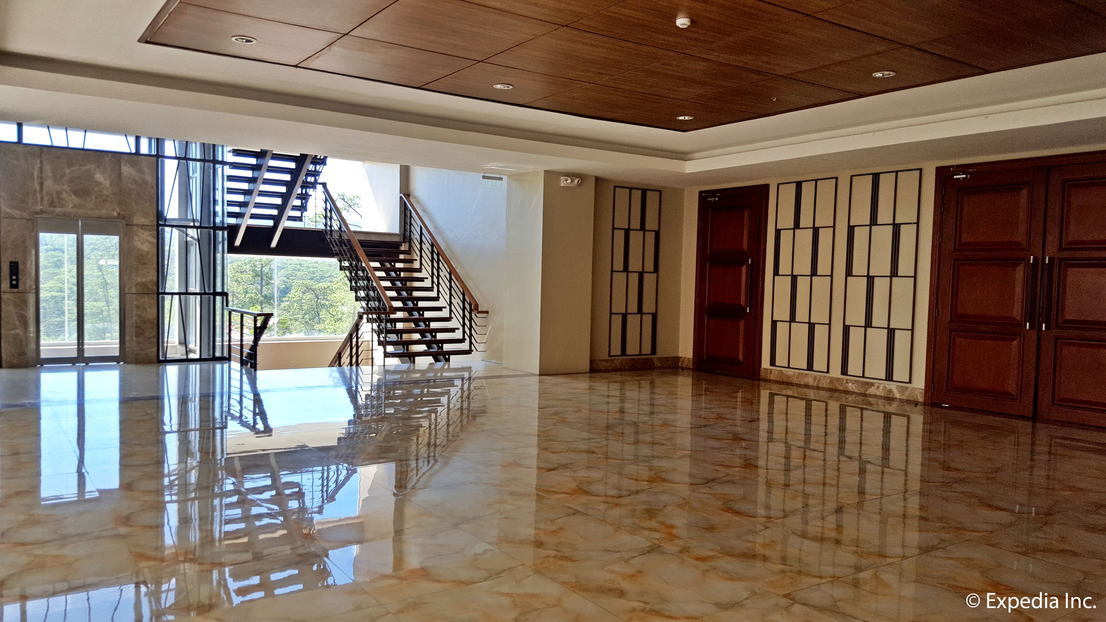 A spacious lobby with a marble floor, a staircase, and large wooden doors.