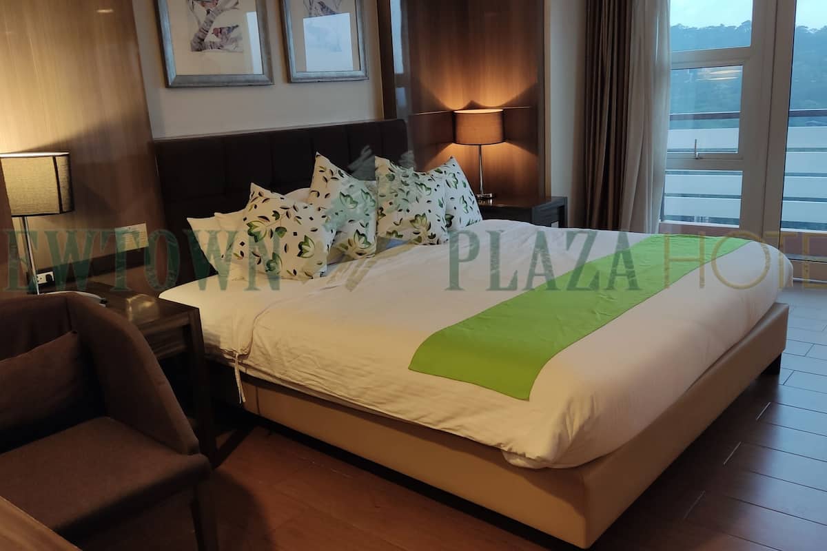 Een hotelkamer met een bed, een stoel, een nachtkastje, een lamp en uitzicht op de omgeving.