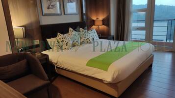 Habitación de hotel con cama, una silla, mesita de noche, lámpara y vistas al exterior.