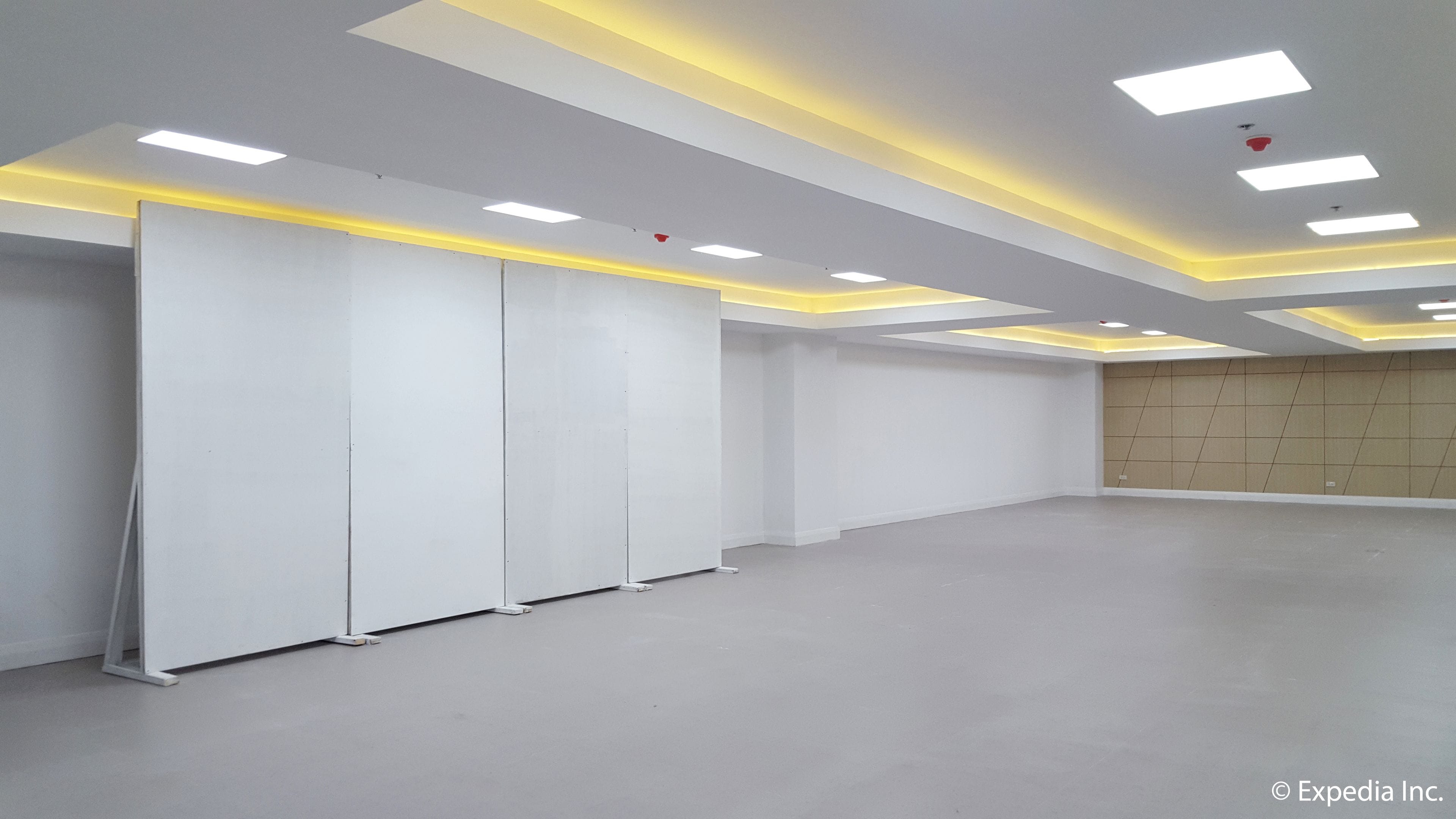 A spacious, modern room with white walls and a grey floor, featuring recessed ceiling lights and a plain, unadorned wall.