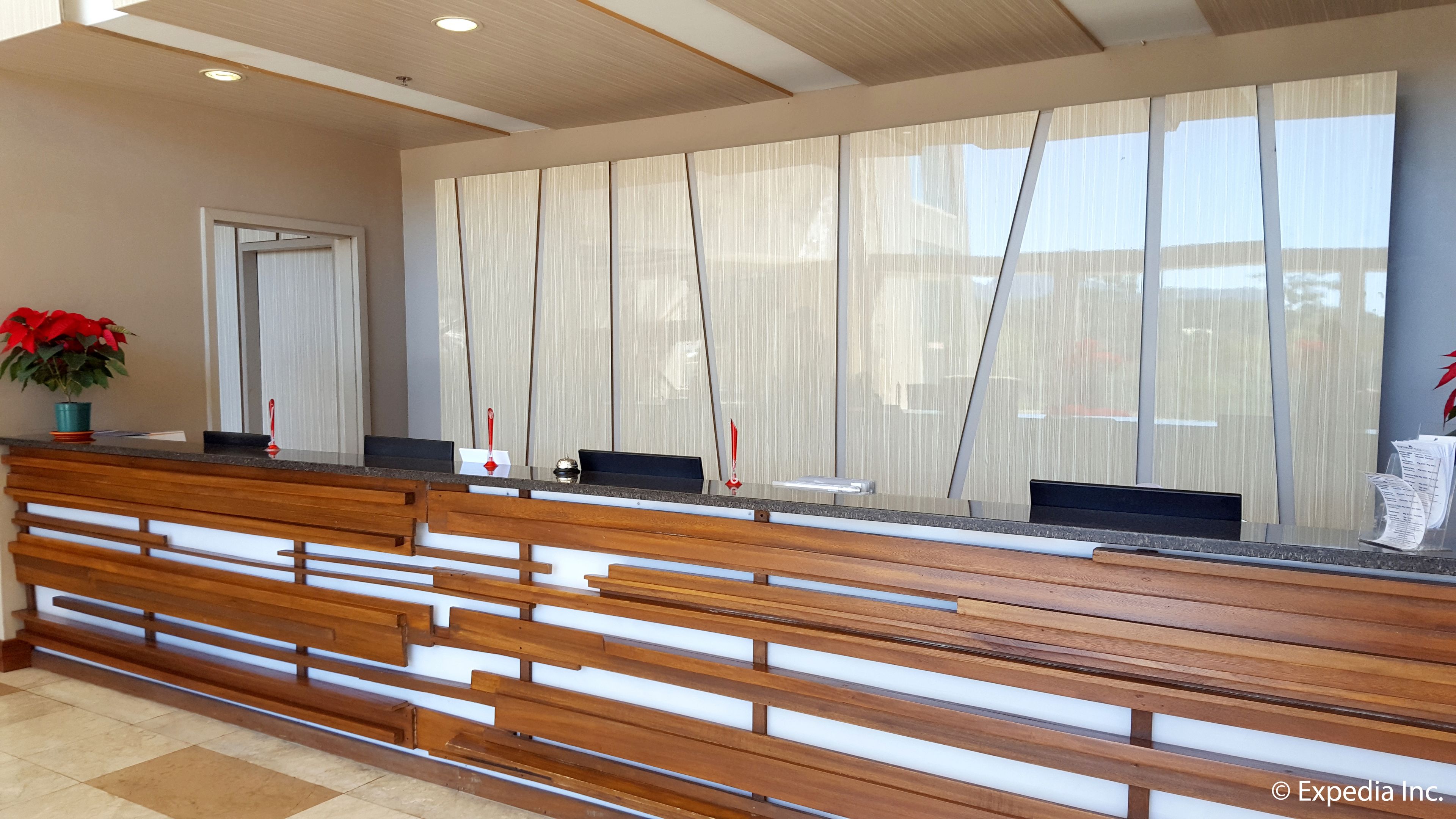 A reception desk with a wooden bench seating area, a potted plant, and a window with sheer curtains.