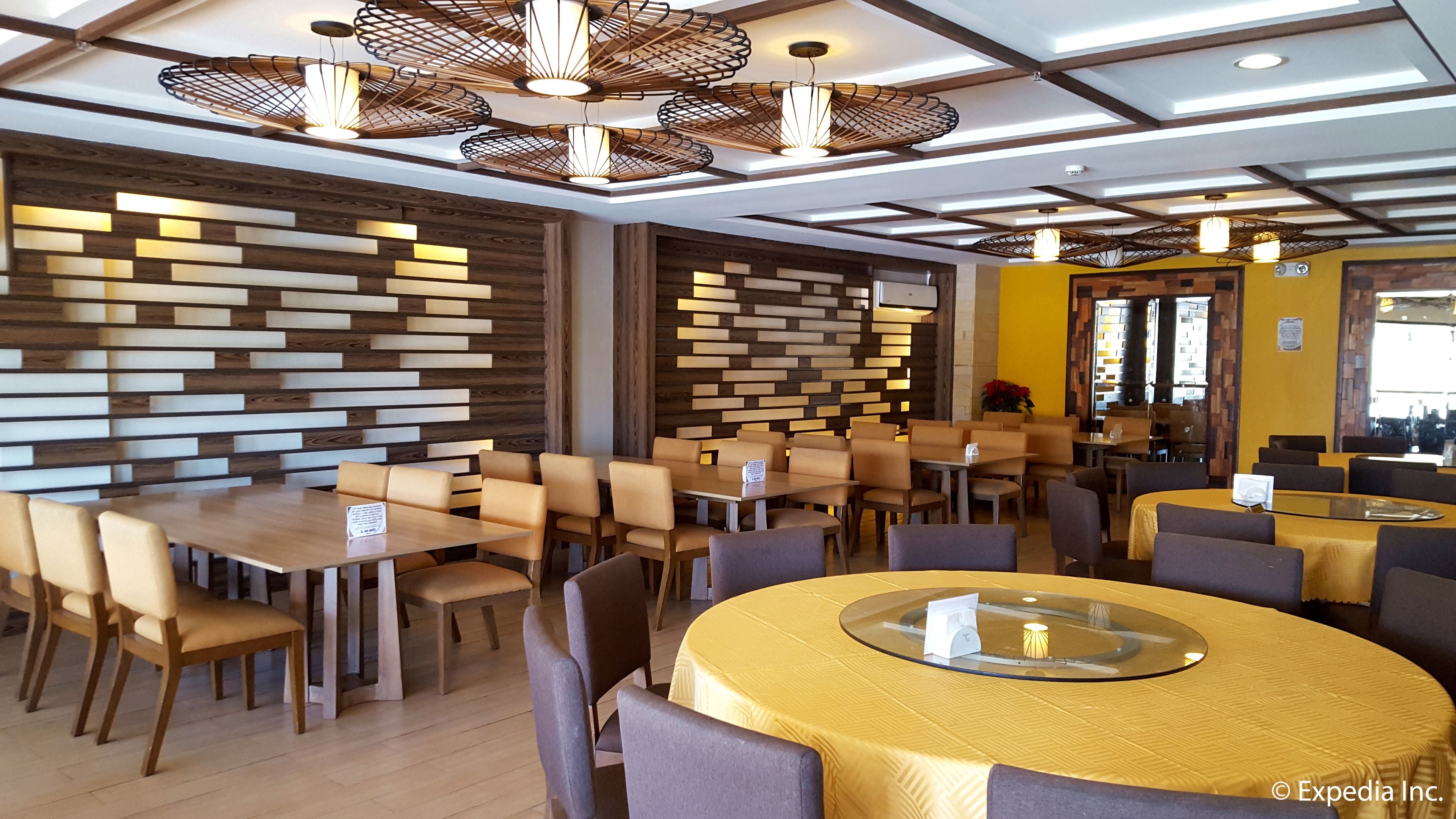 A modern restaurant interior with wooden panel walls, round tables with yellow tablecloths, and unique hanging light fixtures.