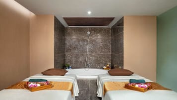 Two single beds with neatly made linens and decorative pillows, a bathtub, and a modern light fixture create a comfortable retreat.