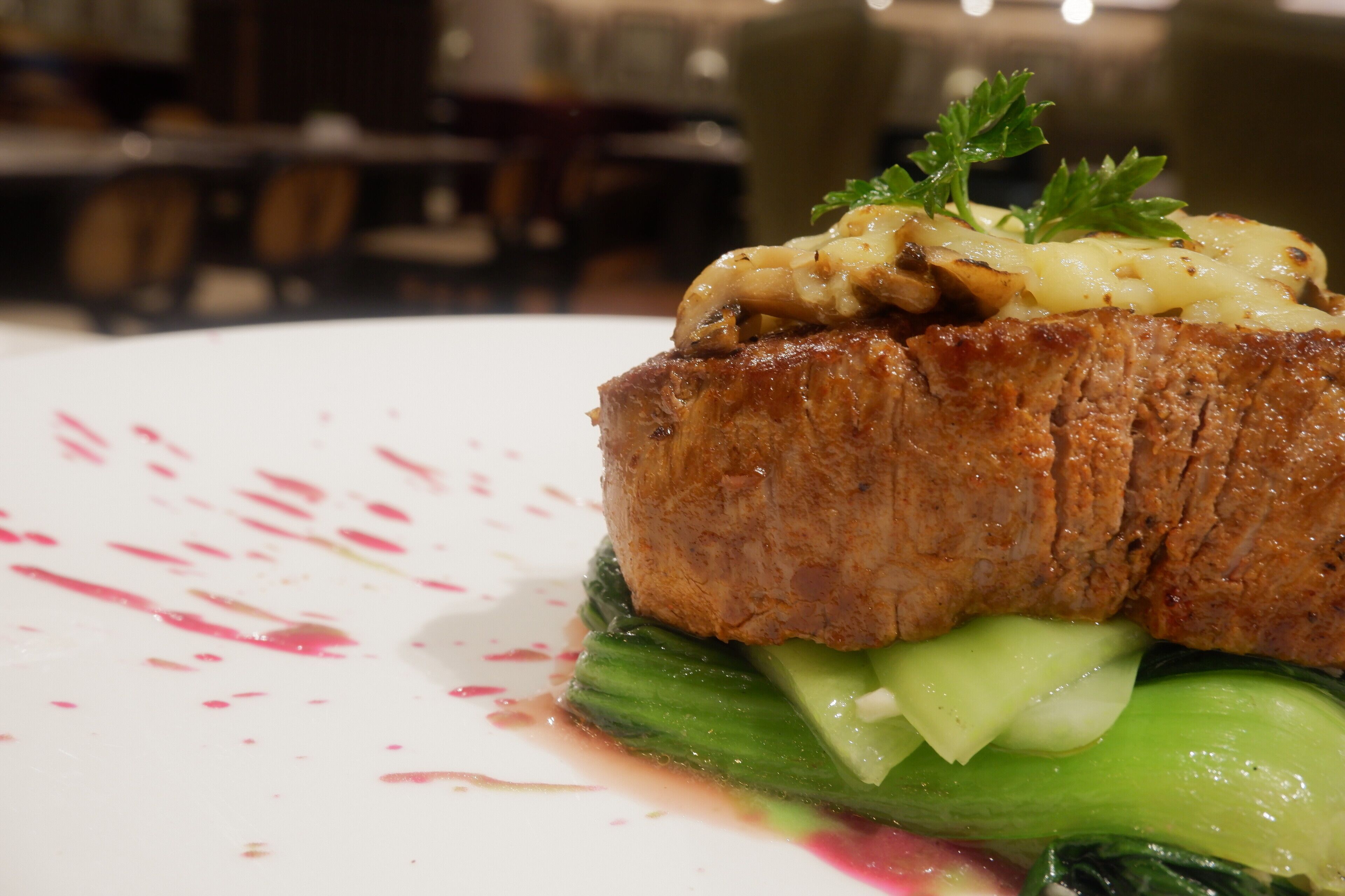 A plated dish with a piece of meat, mushrooms, and greens.
