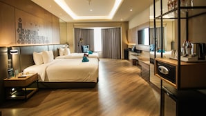 Habitación de hotel con dos camas, un escritorio con computadora, un minibar y un espejo grande.