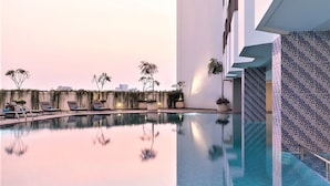Una piscina en la azotea con sillas de descanso, un muro con diseño y cielo despejado.