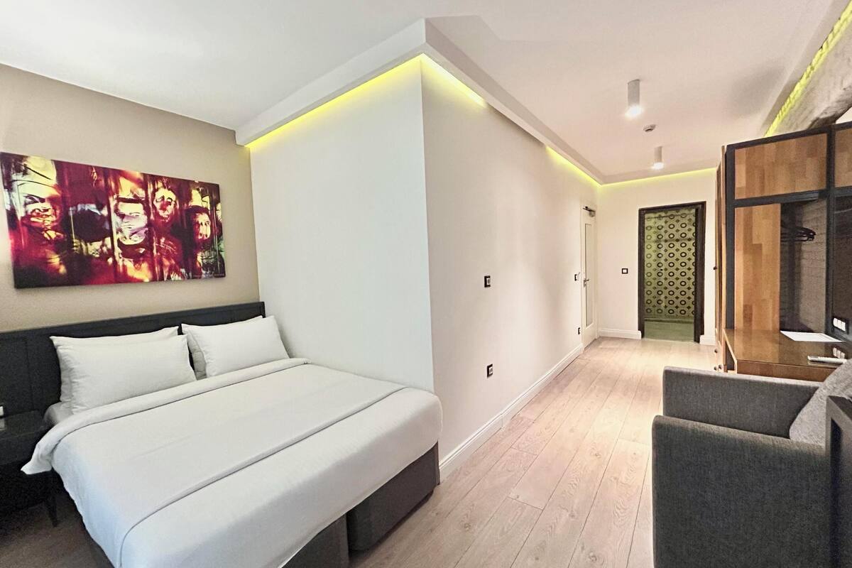 Un dormitorio moderno con una cama grande, un sofá gris, un armario de madera y un cuadro abstracto de colores en la pared.