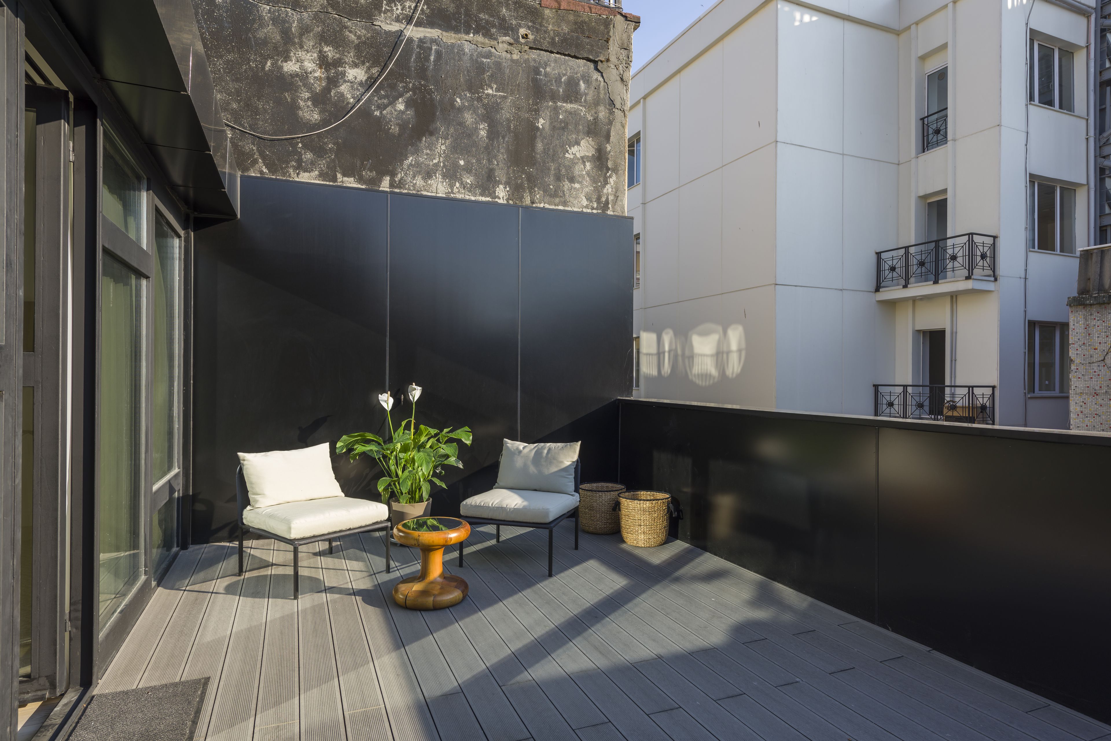 A modern outdoor seating area with a potted plant, two white cushioned chairs, and a wooden table.