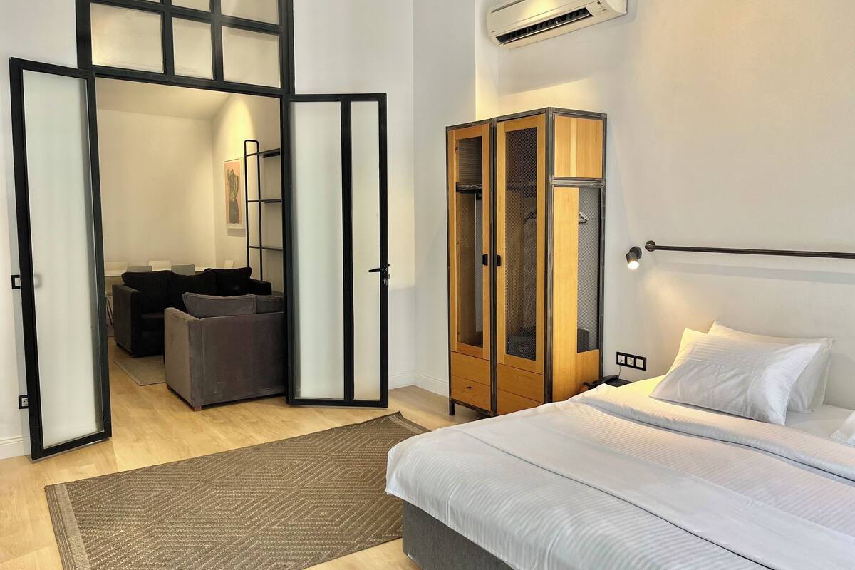 Un dormitorio con cama, armario, zona de estar con sofá y pasillo que conduce a otra habitación.