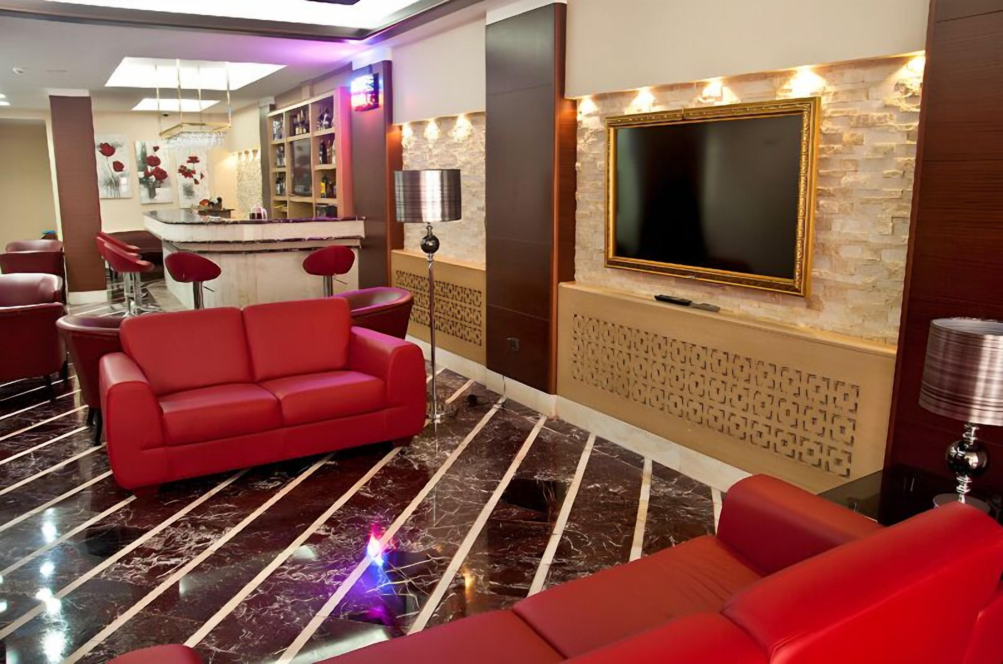 Uma área de estar moderna com um sofá vermelho, um bar com banquetas e uma televisão grande fixada numa parede de tijolos.
