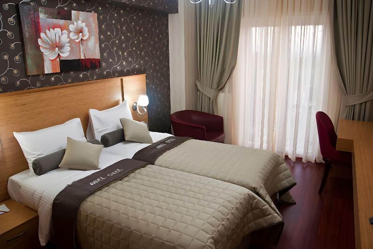 A hotel room with two beds, a wooden headboard, a red chair, a desk, and a large window with curtains.