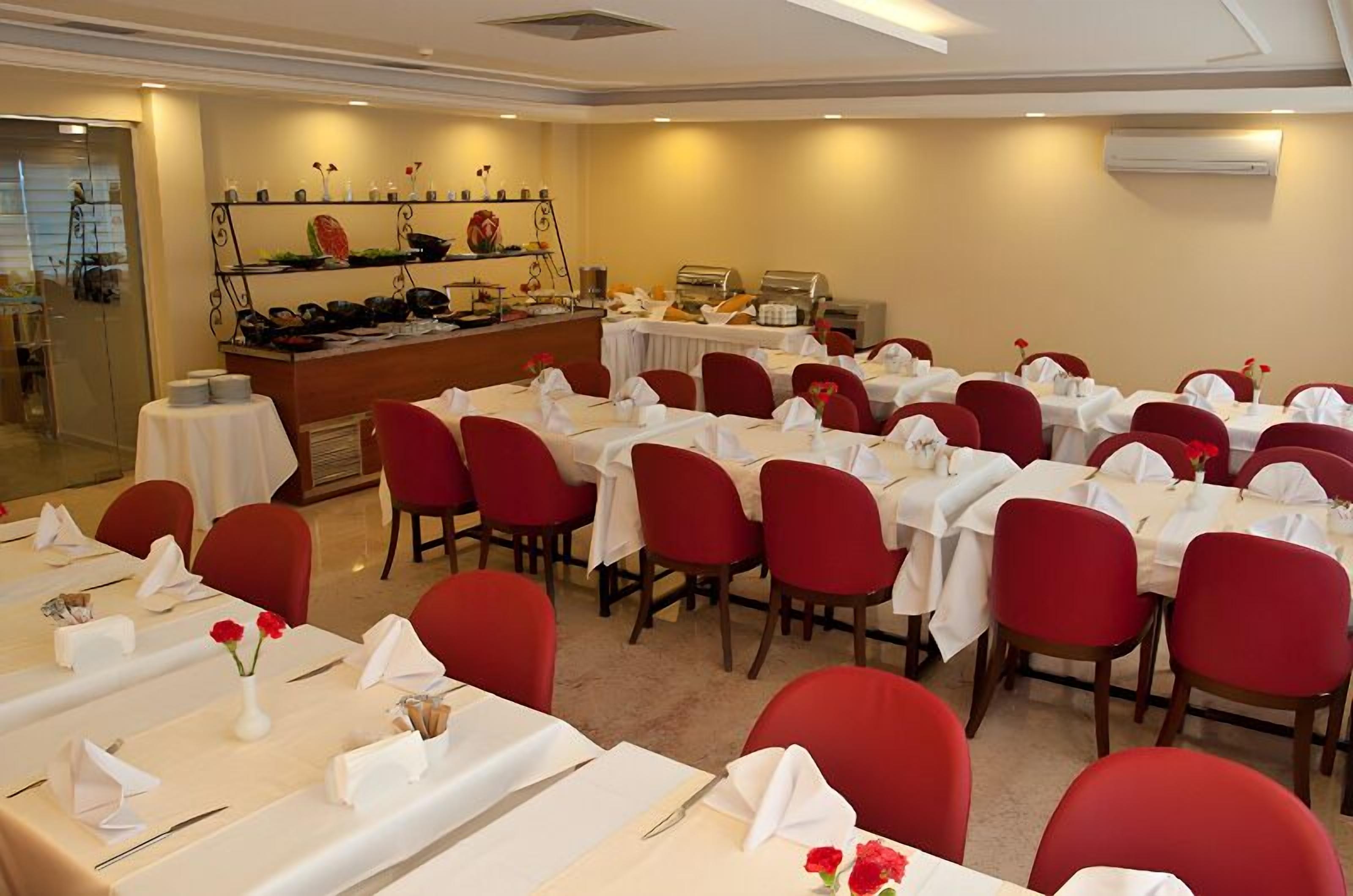 Un salón de banquetes con mesas dispuestas para comer, sillas rojas y una zona de bufé con diversas opciones de comida.