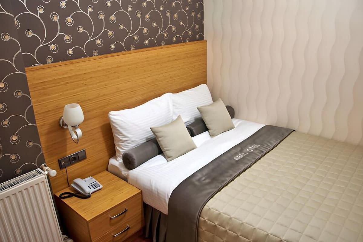 A neatly made bed with a wooden headboard, a bedside table with a telephone, and a wall-mounted lamp.