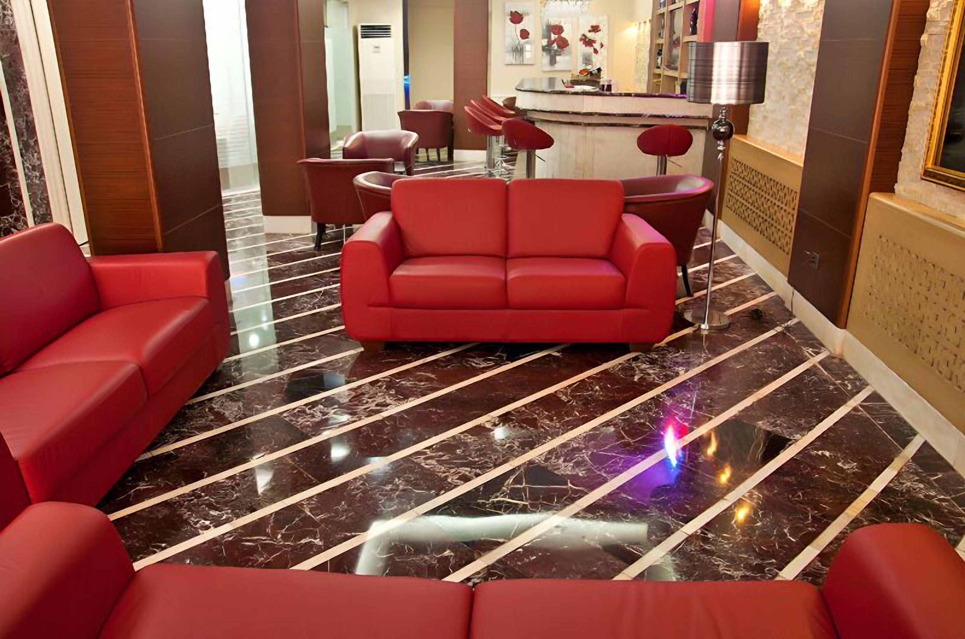 Un moderno vestíbulo de hotel con un conjunto de sofás rojos, una zona de bar y un suelo de mármol.