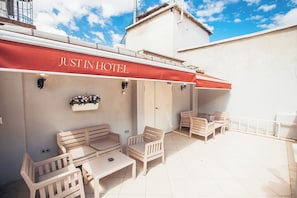 An outdoor seating area with a red awning labeled 'JUSTINHOTEL,' wooden furniture, and a tiled floor. - Just Inn Hotel (Istanbul)