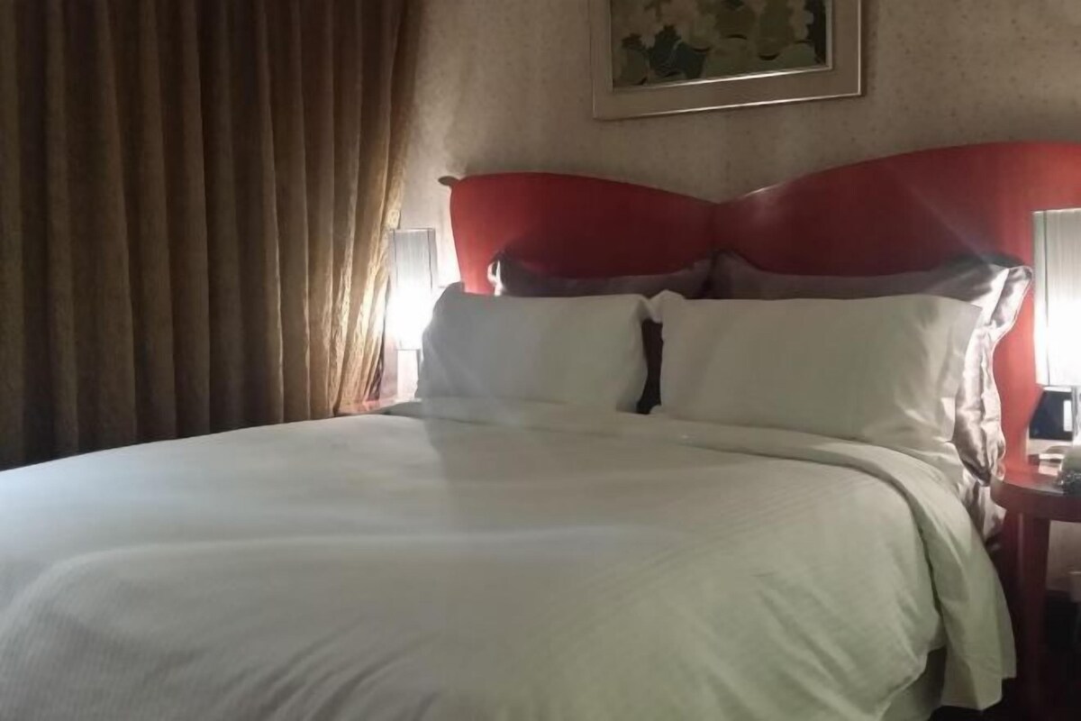 Een hotelkamer met een groot bed, een rode hoofdbord en een schilderij aan de muur.