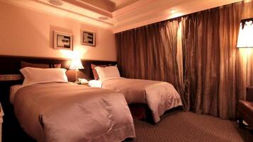 A hotel room with two beds, a large window with curtains, a headboard, and a lamp.