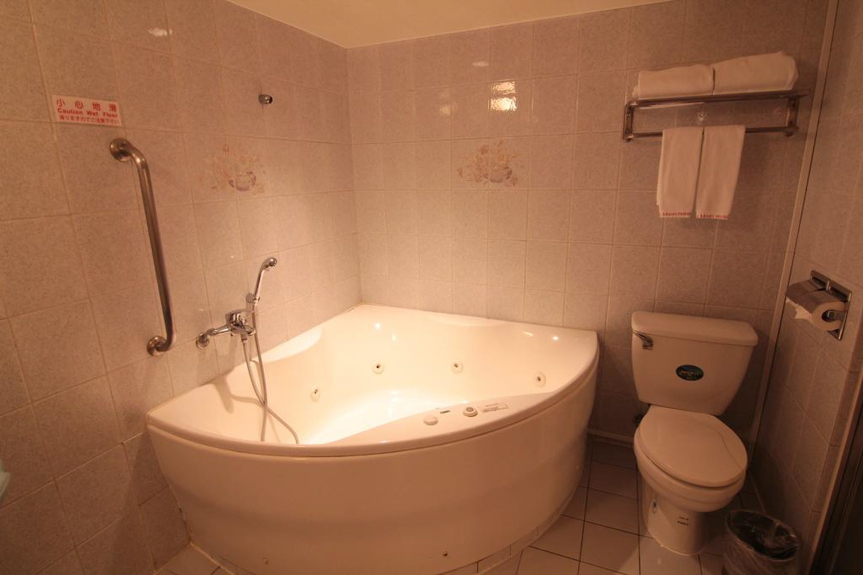 A bathroom with a bathtub, toilet, and a handrail.