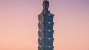 A tall, modern skyscraper with a unique stepped design, surrounded by a cityscape with various buildings and a mountain in the background. - The Moon Hotel (Taipei)