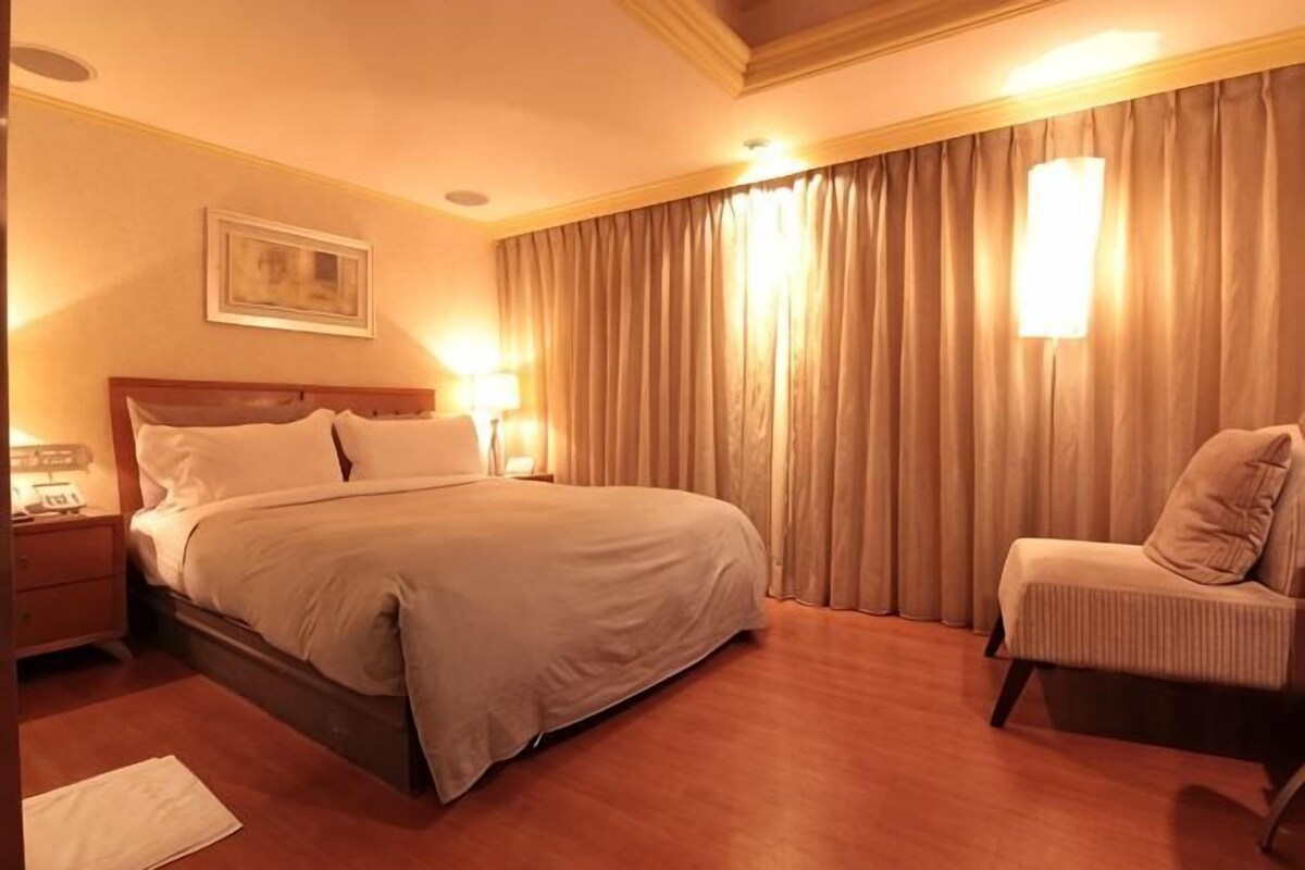 Een hotelkamer met een bed, nachtkastje, lamp en een stoel.