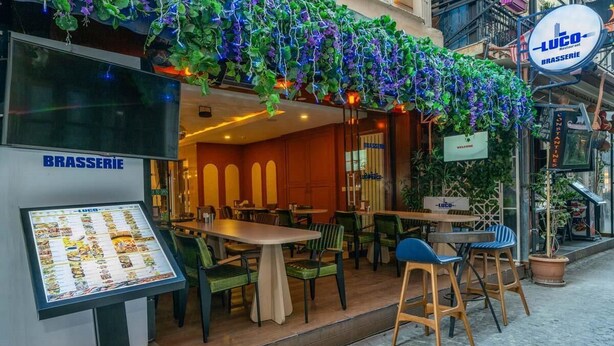Un espace extérieur aménagé avec des tables et des chaises, un panneau affichant le menu et une enseigne pour le restaurant LUCO.