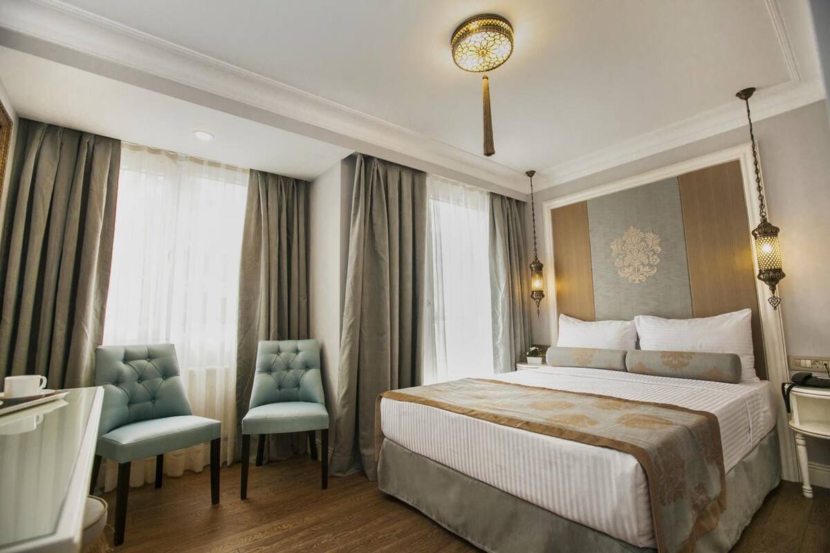 Ein Hotelzimmer mit einem großen Bett, zwei Stühlen, einem Schreibtisch und einem Nachttisch.