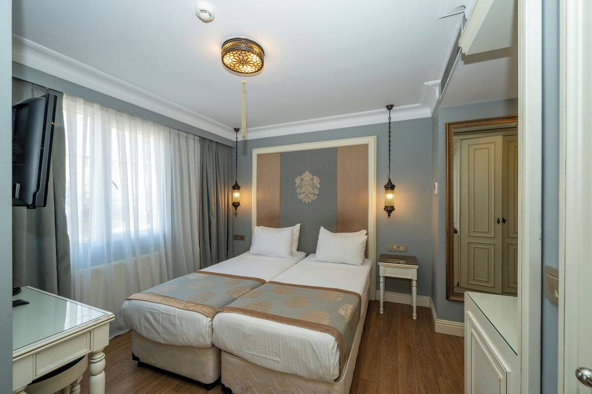 Ein Hotelzimmer mit zwei Betten, einem Schreibtisch, einem Stuhl, einem Nachttisch und einem Spiegel.