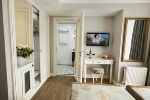 Una habitación de hotel con piso de madera, un tocador blanco con espejo, un televisor montado en la pared y una cama con cubrecama estampado.