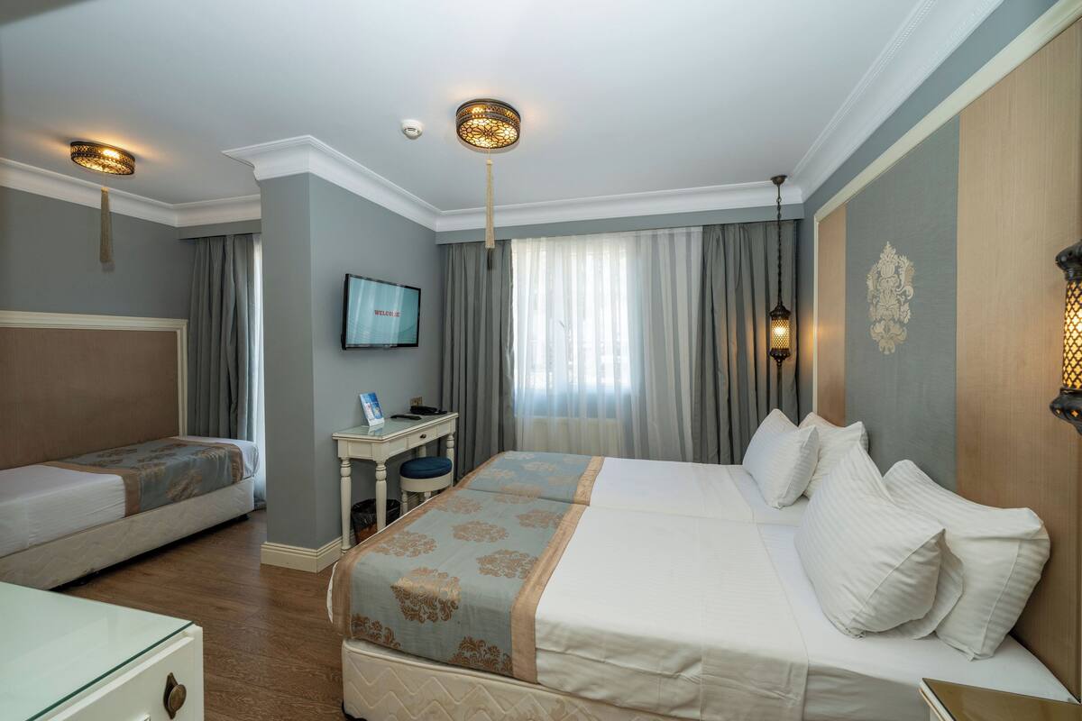 Ein Hotelzimmer mit zwei Betten, einem Schreibtisch, einem Fernseher und einem fenster mit Vorhängen.