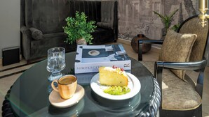 Un salon moderne avec une table basse ronde en verre, un canapé et un fauteuil. On y trouve une suspension bleue, une fresque murale et une petite plante posée sur la table.