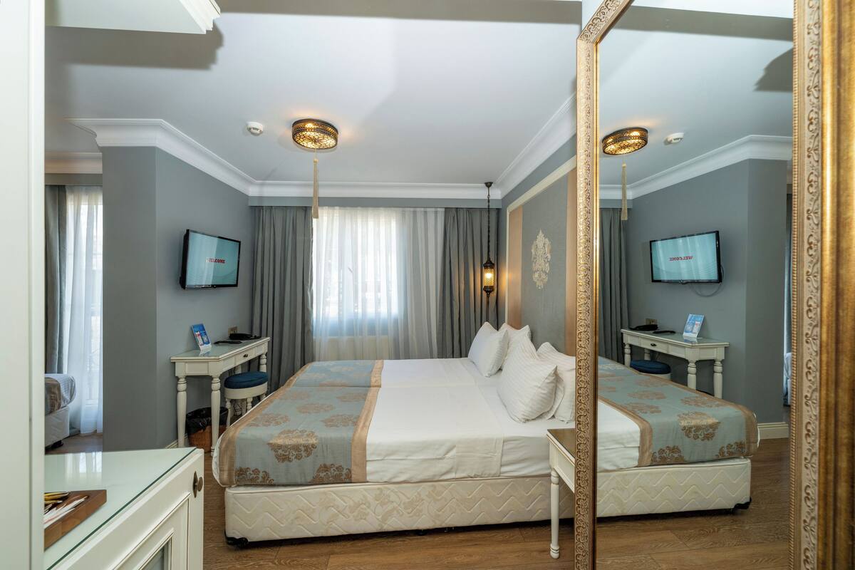 Ein Hotelzimmer mit einem großen Bett, zwei Nachttischen, einem Schreibtisch, einem Sessel und einem Spiegel.