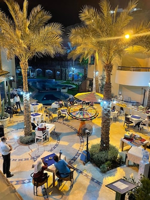 An outdoor dining area with palm trees, a pool, and a colorful circular seating arrangement.