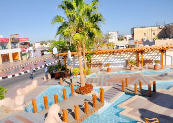 A pool area with a wooden deck, palm trees, and a pergola.