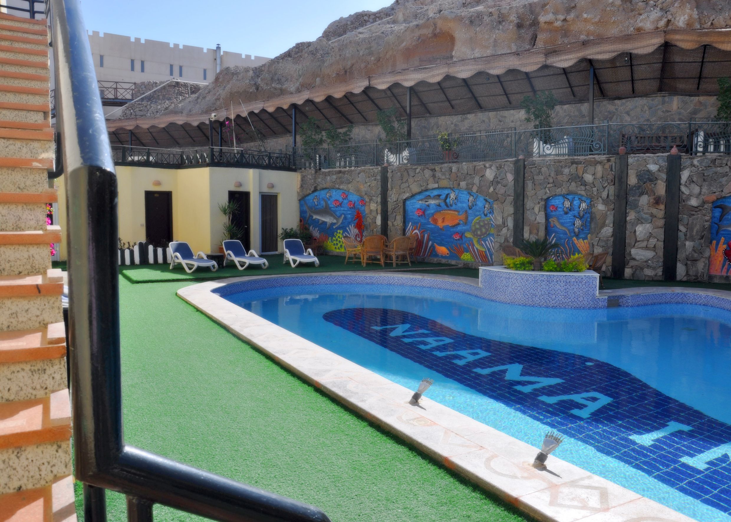 A swimming pool with a tiled edge and a mural of marine life. There are lounge chairs and a stone wall with a mural.