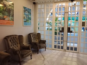 A lobby with two brown upholstered chairs, a large poster on the wall, and a glass door leading outside. - Reggae Mansion Hostel (Kuala Lumpur)