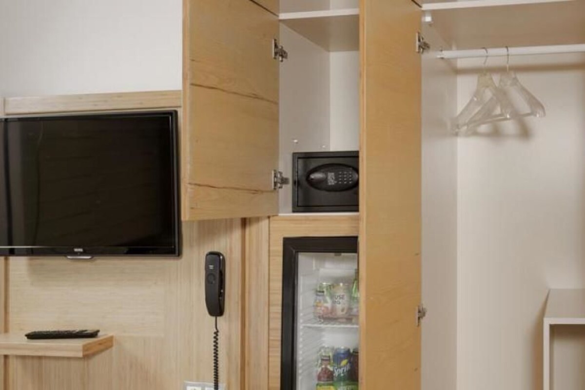 Habitación pequeña con un armario de madera, televisión integrada, teléfono y un refrigerador pequeño.