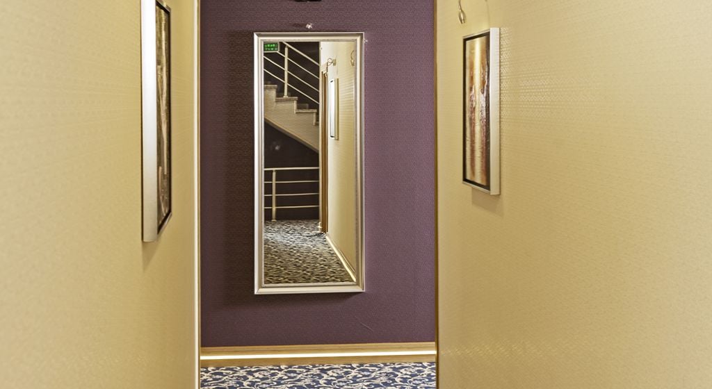 Un pasillo con un espejo que refleja una escalera, cuadros en las paredes y un suelo estampado.
