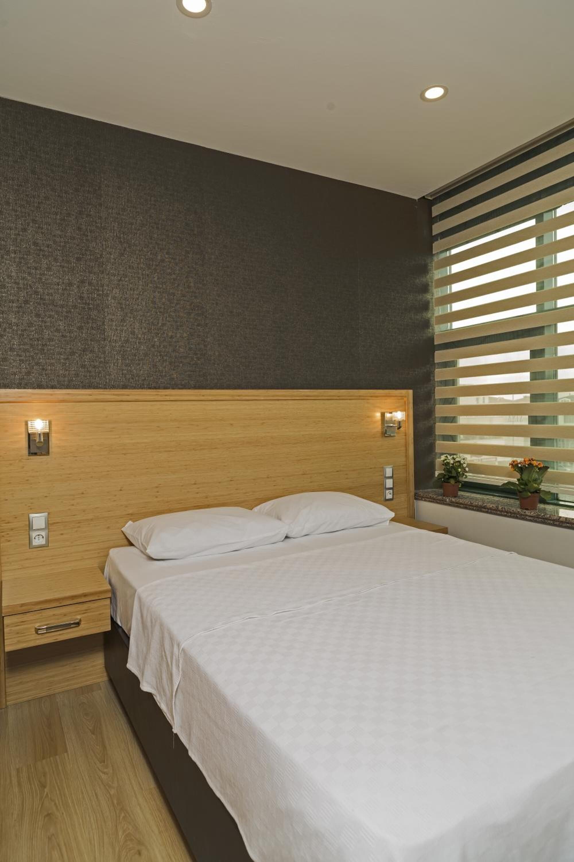Un dormitorio moderno con una cama grande, cabecero de madera, lámparas de noche y una ventana con persianas.