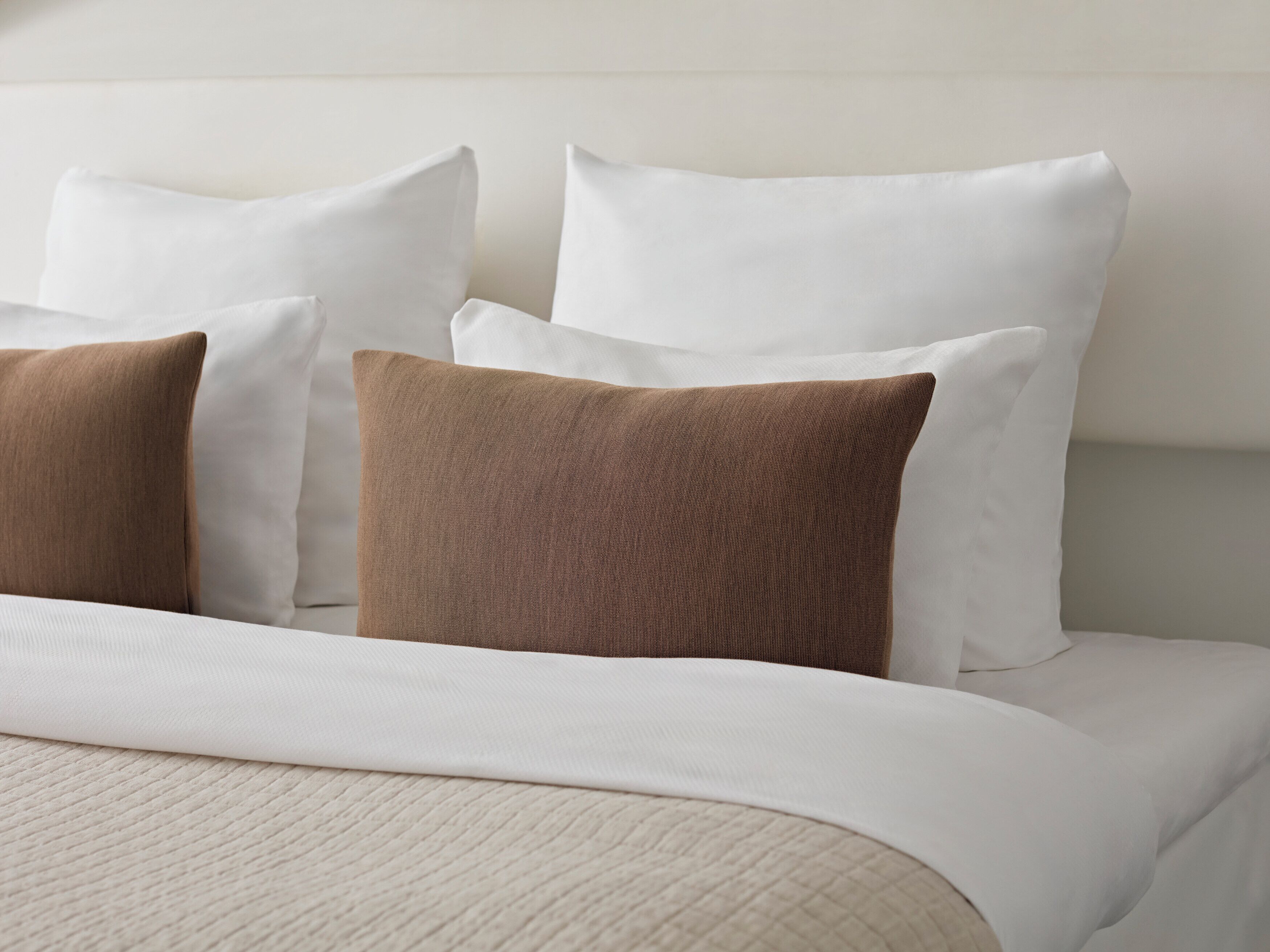 Un lit bien fait, avec des oreillers blancs et bruns, une couette blanche et une couverture à motifs.