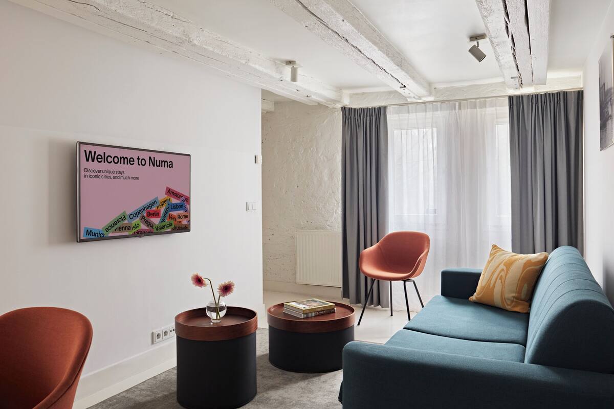 A modern living room with a blue sofa, a red chair, a round coffee table, and a 'Welcome to Numa' sign.