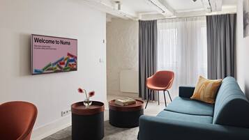 Een moderne woonkamer met een blauwe bank, een rode fauteuil, een ronde salontafel en een bordje met de tekst 'Welcome to Numa'.